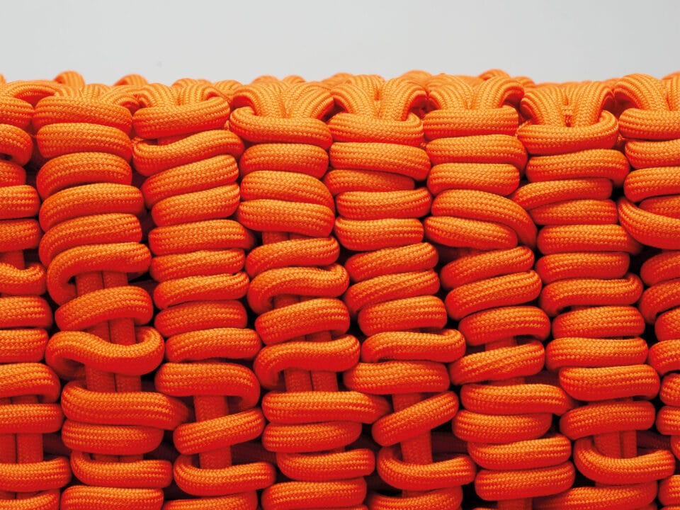 a detail of a large knitted surface made of orange nylon rope