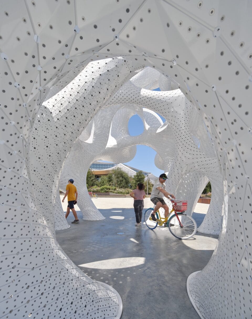 people move around inside of a contemporary white architectural pavilion with undulating forms in the overall shape of a sphere