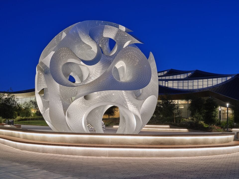 a contemporary white architectural pavilion with undulating forms in the overall shape of a sphere, pictured illuminated at night